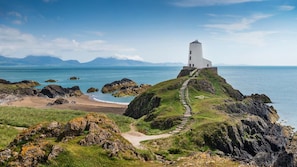 Un phare situé sur une côte rocheuse, offrant une vue dégagée sur la mer et les montagnes lointaines.