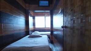 A narrow corridor with two beds, wooden walls, and a window at the end.