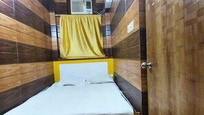 A narrow hotel room with a bed, a yellow curtain, and a wall-mounted air conditioner.