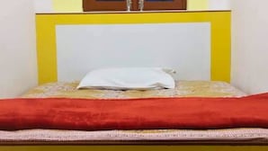 A bed with a white pillow, a red blanket, and a yellow headboard.