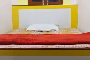 A bed with a white pillow, a red blanket, and a yellow headboard.