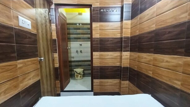 Ett hotellrum med en väggpanel i trä, en synlig dörr och en liten hink på golvet.