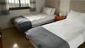 Een hotelkamer met twee bedden, een raam met gordijnen, een nachtkastje met een lamp en een aan de muur hangend schilderij.