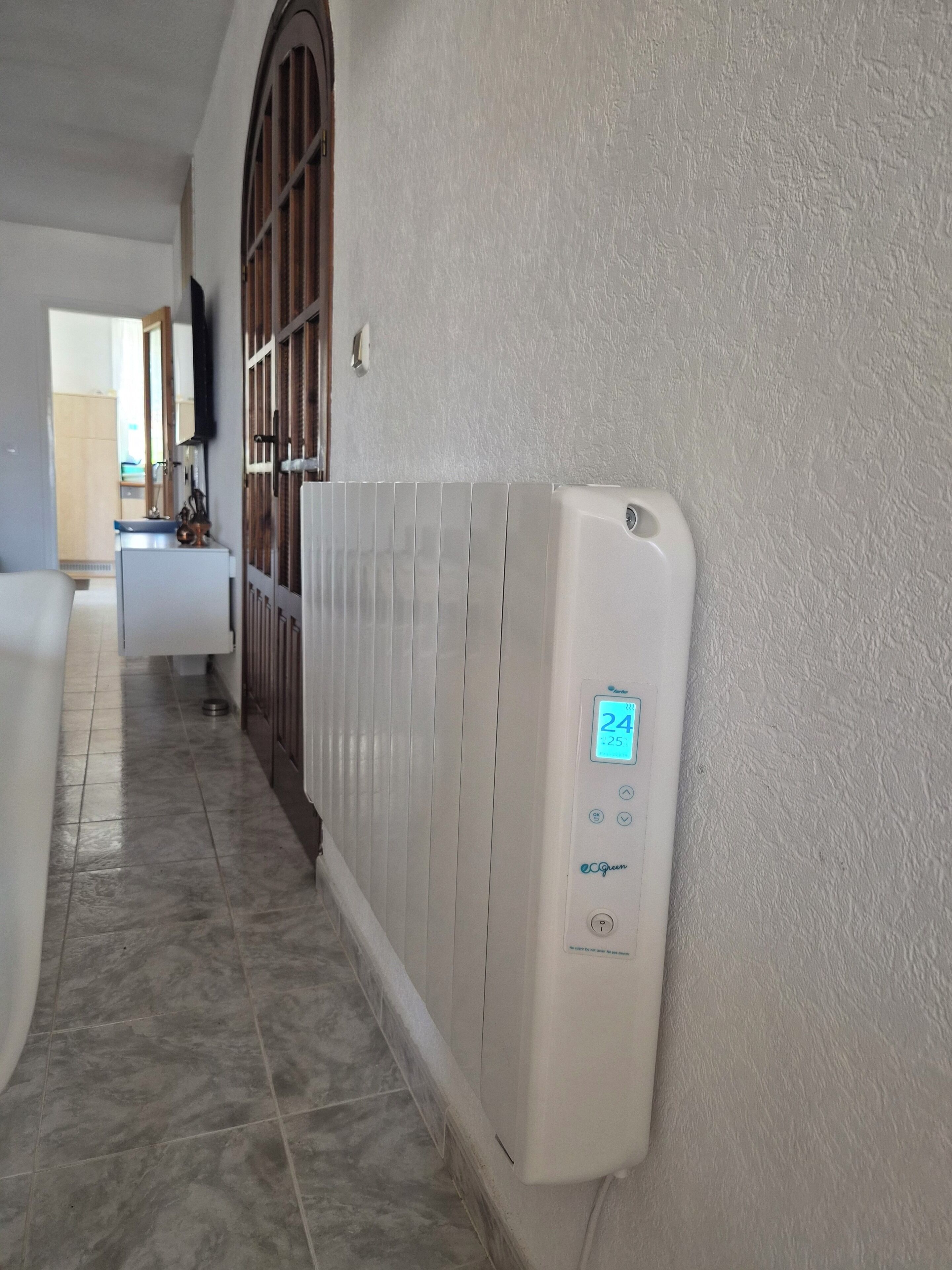 Un pasillo con un radiador blanco, suelo de baldosas y una puerta que da a otra habitación.