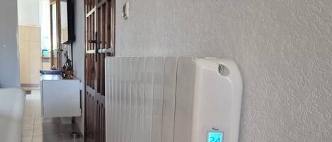 Un pasillo con un radiador blanco, suelo de baldosas y una puerta que da a otra habitación.