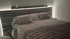 Una cama con cabecera a rayas, una mesita de noche y una lámpara fijada a la pared.