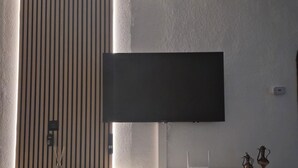 Una sala moderna con un televisor de pantalla plana montado en una pared blanca, un panel de pared texturizado, una mesita con un plato decorativo y un tapete tejido.