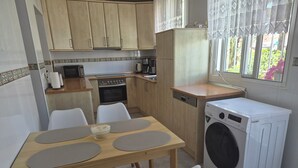 Una cocina compacta con lavadora, una mesa de comedor con sillas y un ventanal con cortinas estampadas.