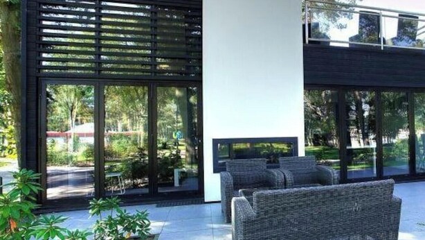A modern outdoor seating area with a sofa and a table, surrounded by glass doors and a black fence. - Holiday Home in Otterlo With Terrace (Otterlo)