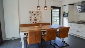 A modern kitchen with a wooden dining table, four chairs, pendant lights, and a view of the outdoors. - Holiday Home in Otterlo With Terrace (Otterlo)
