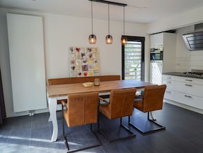 Eine moderne Küche mit Holzesstisch, vier Stühlen, Pendelleuchten und Blick ins Freie.