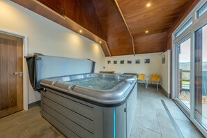 A spa room with a hot tub, wooden ceiling, and large windows. - Luxury holiday cottage with an indoor hot tub West Wales | Golwg-Y-Cwm (Llanfyrnach)
