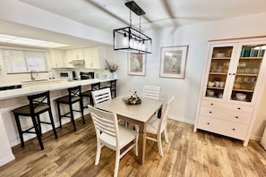 Eine moderne Küche mit weißen Schränken, einem Holztisch und einem gläsernen Schrank mit Geschirr.