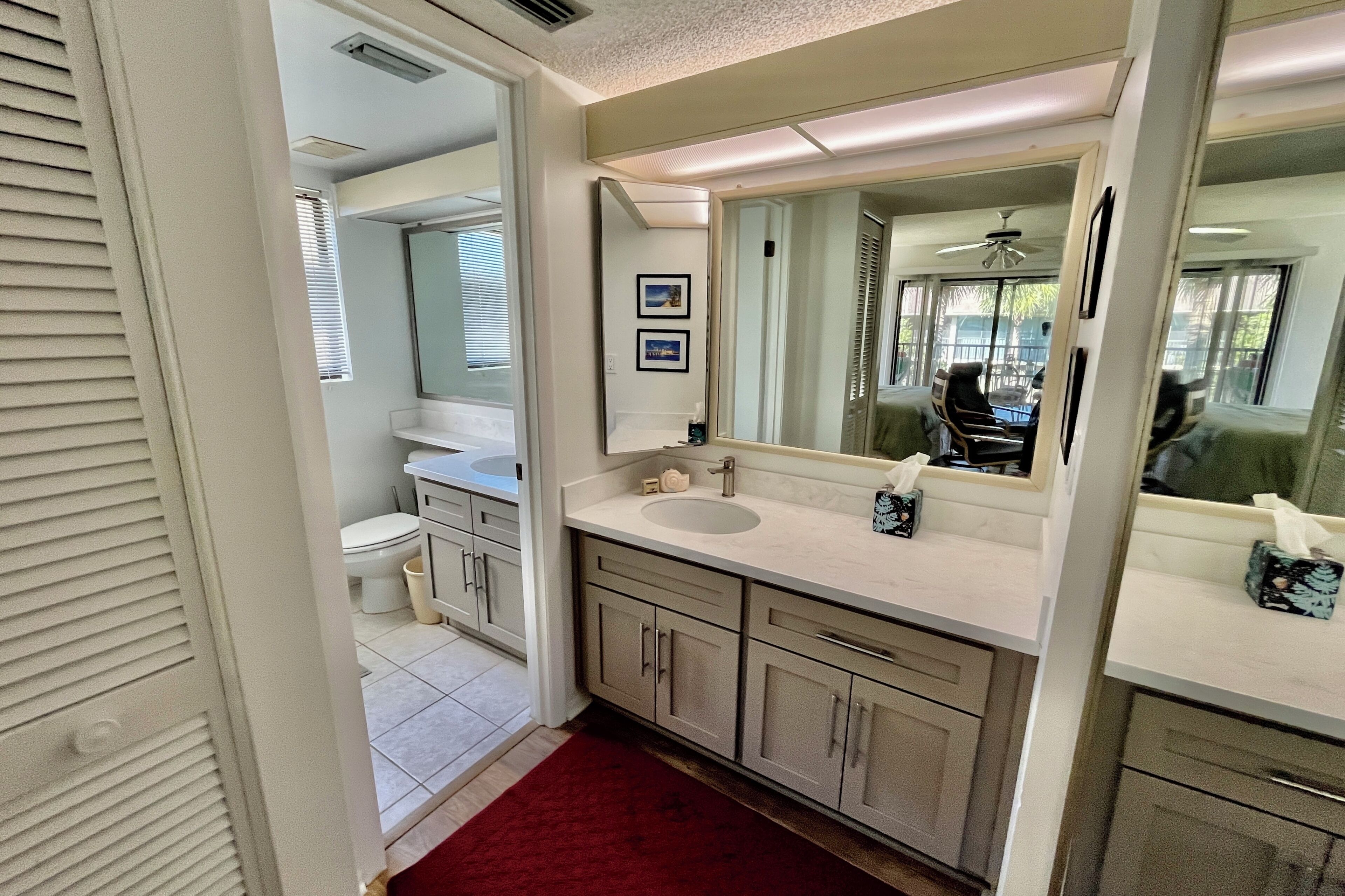 A bathroom with a double sink, a large mirror, and a red rug.