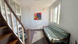 Una escalera con barandilla de madera, un banco con cojín a rayas, un cuadro abstracto y colorido en la pared y una ventana con cortinas.