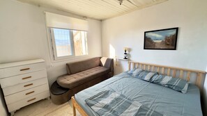 A bedroom with a bed, a sofa, a dresser, a window, and a painting on the wall.