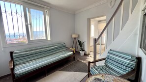 Ein Zimmer mit einer Bank, einer Stehlampe, einer Topfpflanze und Blick durch ein Fenster.