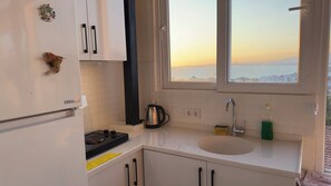 A kitchen with a stove, kettle, sink, and a window with a view.
