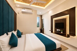 Un dormitorio moderno con cama, almohadas color turquesa, televisor montado y ventilador de techo.