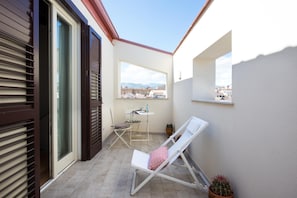 Ein Balkon mit einem weißen Stuhl, einem kleinen Tisch und einem Blumentopf.