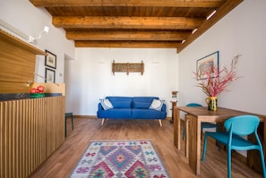 Ein Zimmer mit Holzboden, einem blauen Sofa, einem Holztisch und einem gemusterten Teppich.
