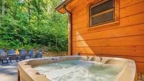Eine Holzblockhütte mit Whirlpool, Sitzgelegenheit im Freien und einem Wald im Hintergrund.