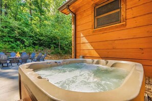 Eine Holzblockhütte mit Whirlpool, Sitzgelegenheit im Freien und einem Wald im Hintergrund.