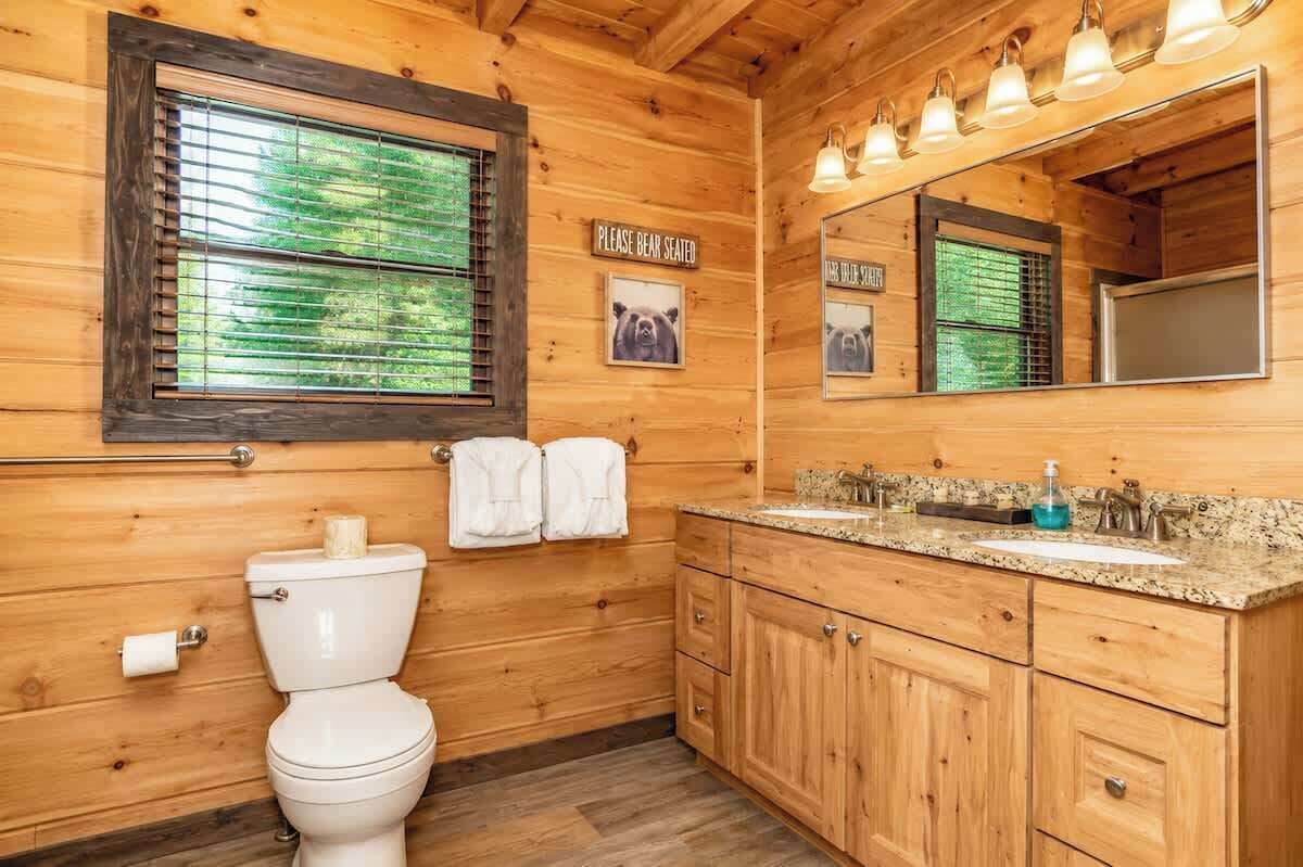 A wooden cabin bathroom with a toilet, sink, cabinets, and a mirror.