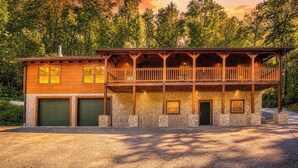 Eine zweistöckige Blockhütte mit Balkon, Stein Fundament und zwei Garagentoren.