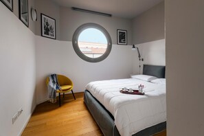 Ein Schlafzimmer mit einem Bett, einem Rundfenster, einem Sessel und einem Nachttisch mit Tablett.