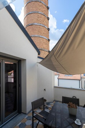 Eine Terrasse mit Tisch und Stühlen, einem beigen Sonnendach und einem Ziegelkamin.