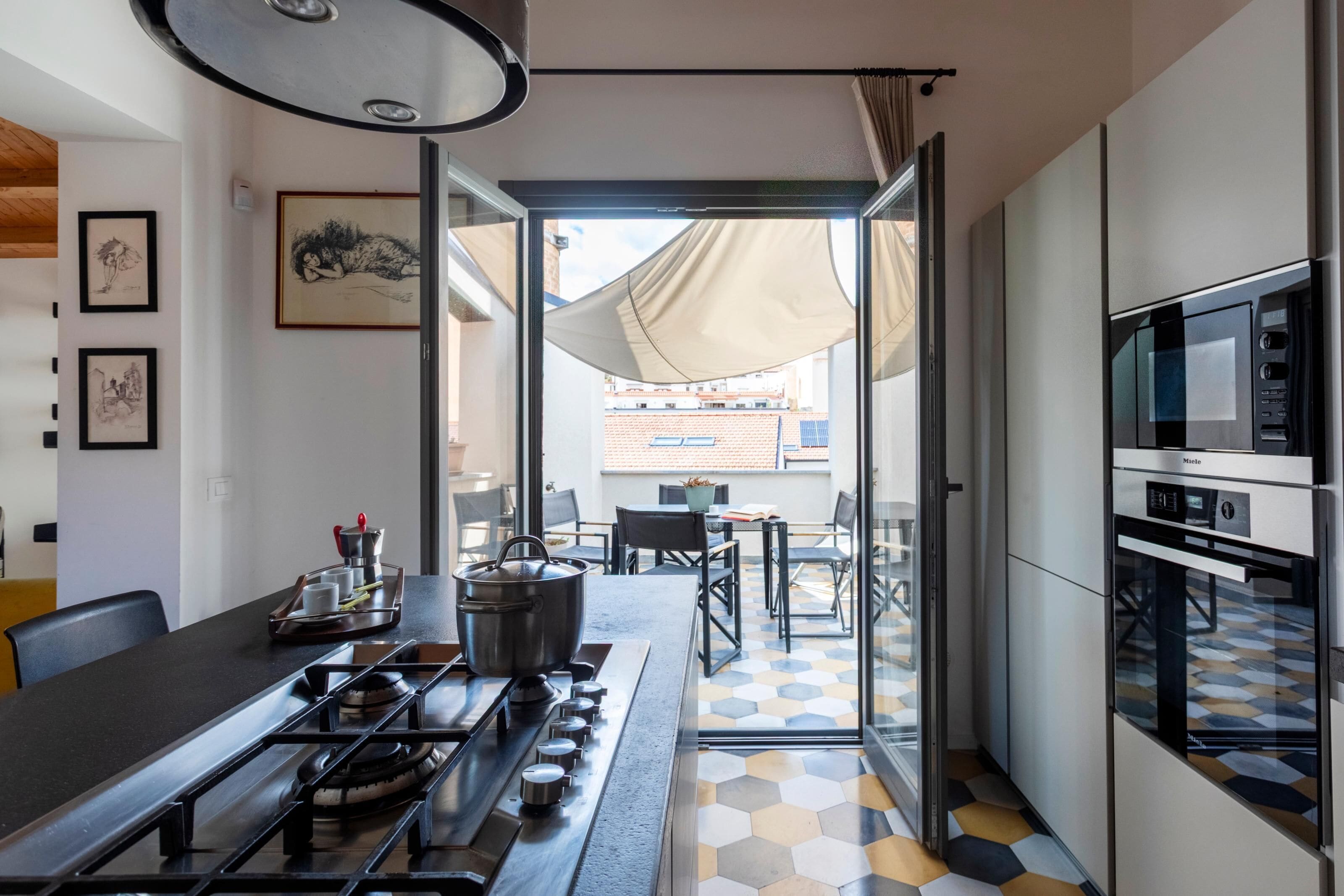 Een moderne keuken met een gasfornuis, magnetron en oven. Er is een eethoek met een tafel en stoelen, en een uitzicht door de glazen deur op een terras.