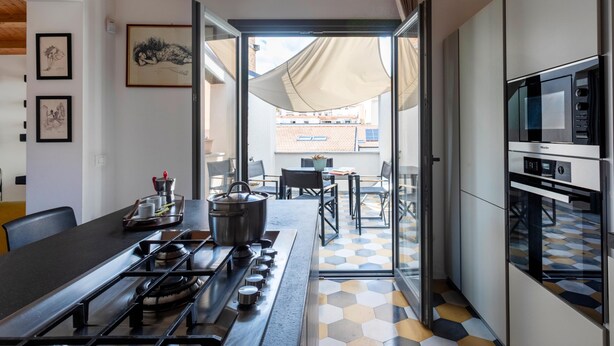 Eine moderne Küche mit Gasherd, Mikrowelle und Backofen. Ein Essbereich mit Tisch und Stühlen lädt zum Verweilen ein, und durch die Glastür bietet sich ein Blick auf eine Terrasse.