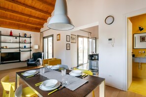 Un comedor con una mesa de madera dispuesta para cuatro personas, una silla negra y un sillón amarillo.