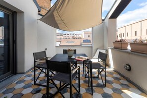 Un balcón con una mesa, sillas, una planta en maceta y vistas a edificios.
