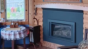 A wooden cabin interior with a fireplace, a table with a tablecloth, a dog, and a leopard print chair. - Blū House. (Williamsburg)