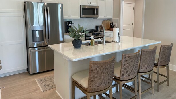A modern kitchen with stainless steel appliances, a central island with bar stools, white cabinetry, and pendant lighting. - Open the Doors to Paradise in This Stunning New Retreat! (Sumterville)