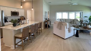 A modern kitchen with a central island, dining area with chairs, a sofa, and a ceiling fan. - Open the Doors to Paradise in This Stunning New Retreat! (Sumterville)