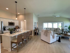 A modern kitchen with a central island, dining area with chairs, a sofa, and a ceiling fan. - Open the Doors to Paradise in This Stunning New Retreat! (Sumterville)