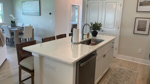 A kitchen with a central island, a dining area with chairs, a potted plant, and a view into another room. - Open the Doors to Paradise in This Stunning New Retreat! (Sumterville)