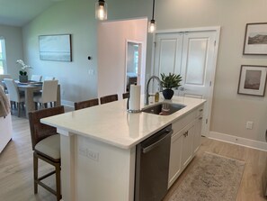 A kitchen with a central island, a dining area with chairs, a potted plant, and a view into another room. - Open the Doors to Paradise in This Stunning New Retreat! (Sumterville)