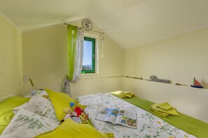 Ein Schlafzimmer mit einem Bett, einem Fenster mit Vorhängen, einer Wanduhr, einem Regal mit Dekoration und einem kleinen Modell eines Segelbootes.