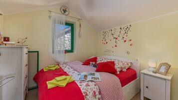 A bedroom with a bed, a bedside table, a nightstand, a window with curtains, a wall clock, and a wall decoration.