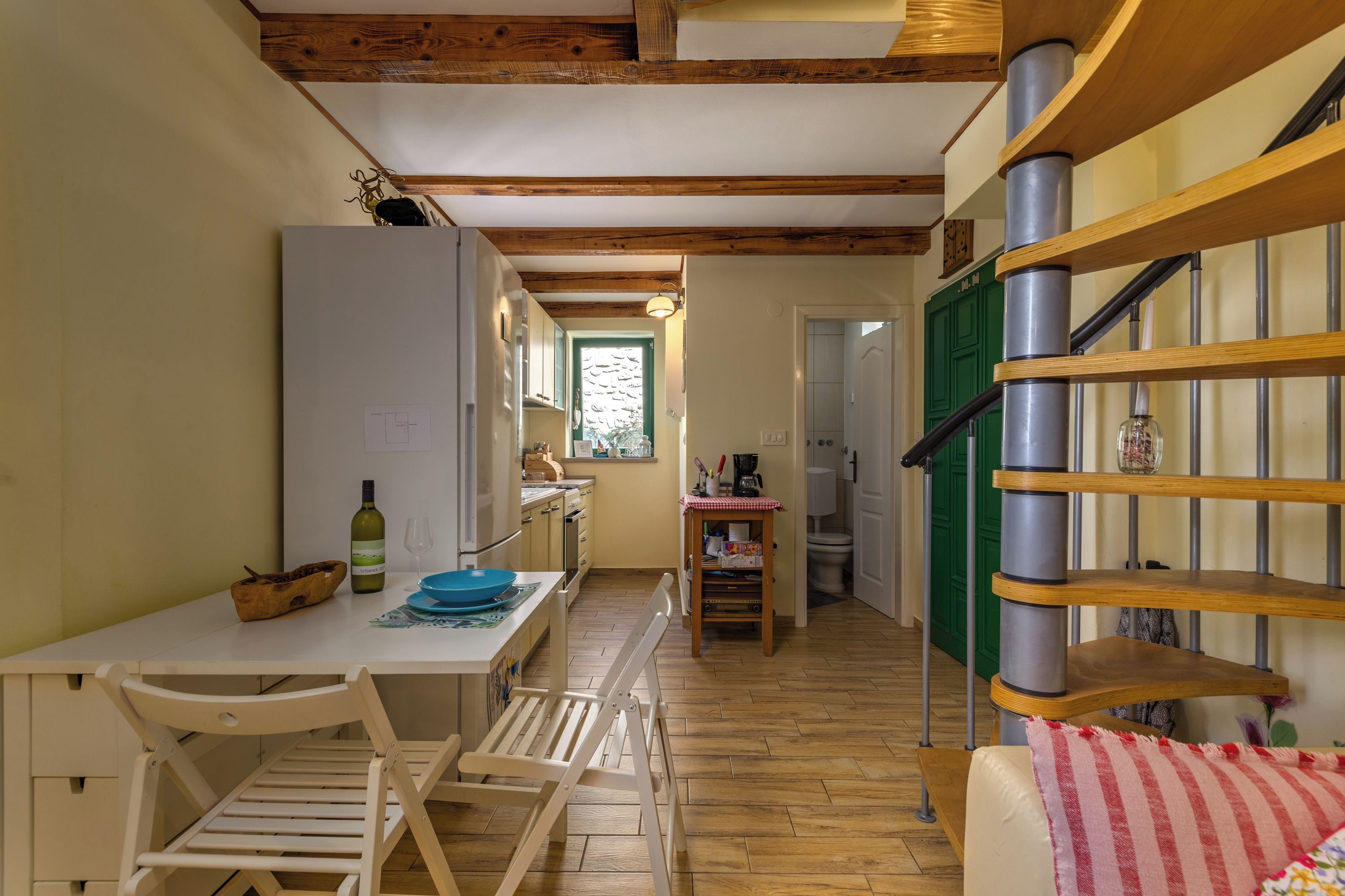 A kitchen with wooden beams, a white table, chairs, and a dining area.