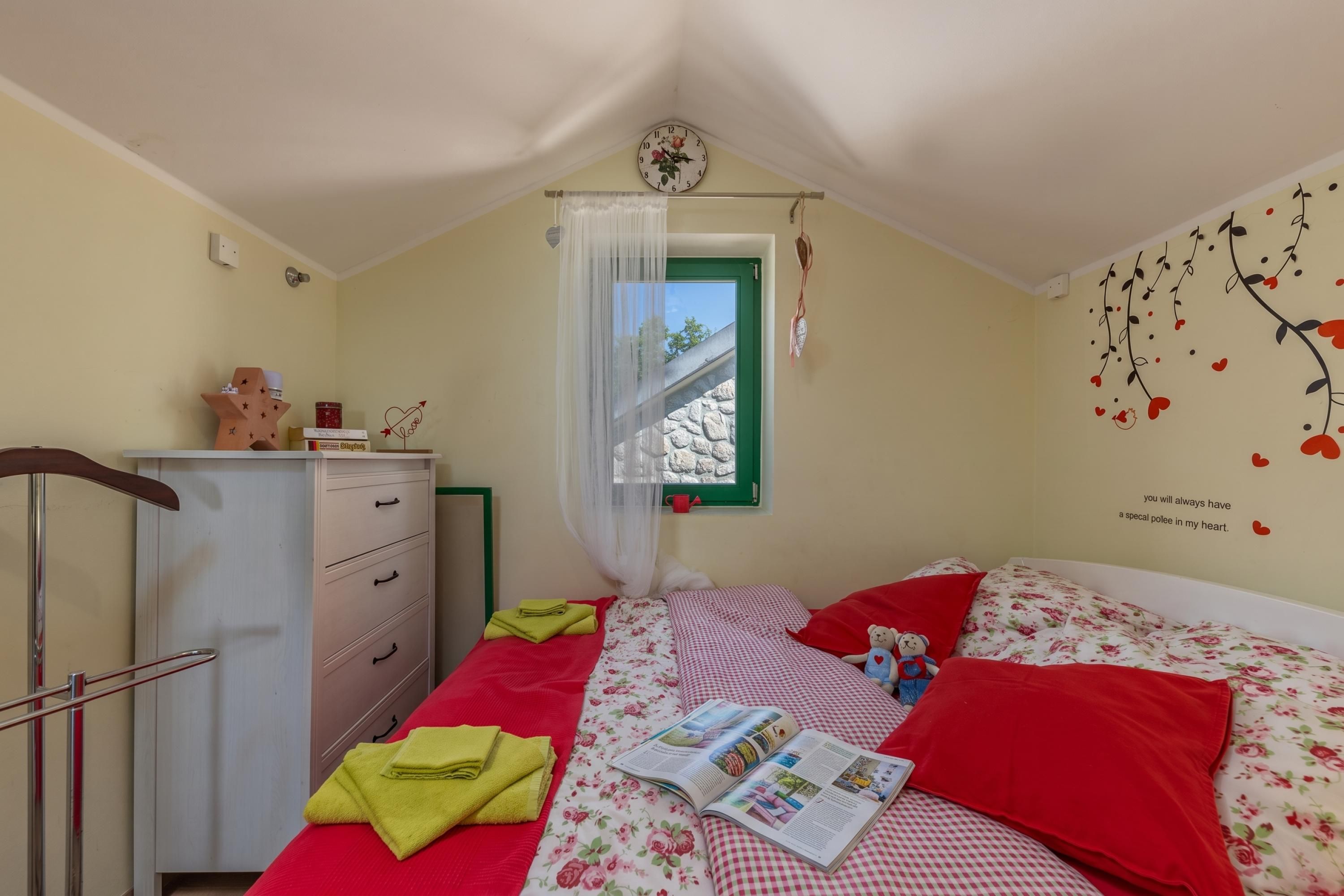 A bedroom with a bed, a bedside table, a wardrobe, a window with a view, and a wall decoration.