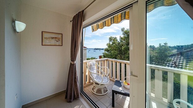 Un balcón con vista al mar, un cuadro enmarcado en la pared y una mesa con sillas.