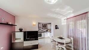 Una sala de estar moderna con televisor, mesa de comedor y sillas, que da paso a una cocina y un baño.