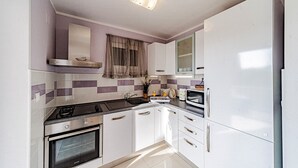 Una cocina compacta con estufa a gas, horno, alacenas blancas y microondas.