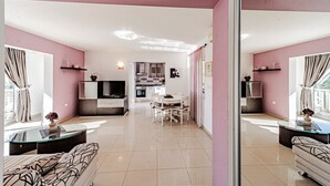Una sala de estar moderna con un sofá, un comedor con sillas, una cocina con televisor y un balcón con cortinas.