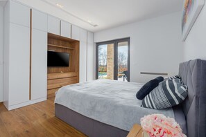 Ein Schlafzimmer mit Bett, Fernseher, Glastür zum Balkon und einem Holzschrank.